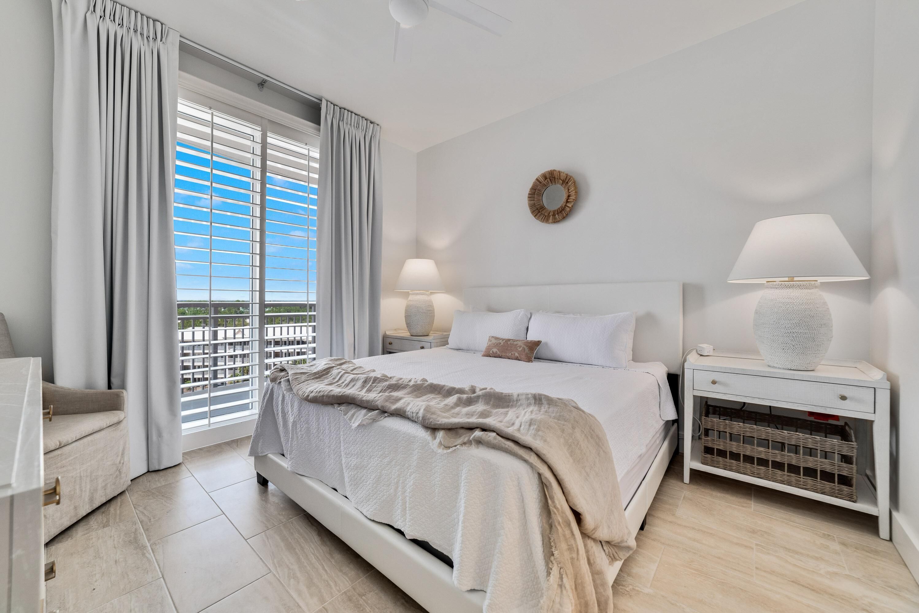 A bedroom with a bed, bedside tables, a nightstand, a window with curtains, and a view of the outdoors.
