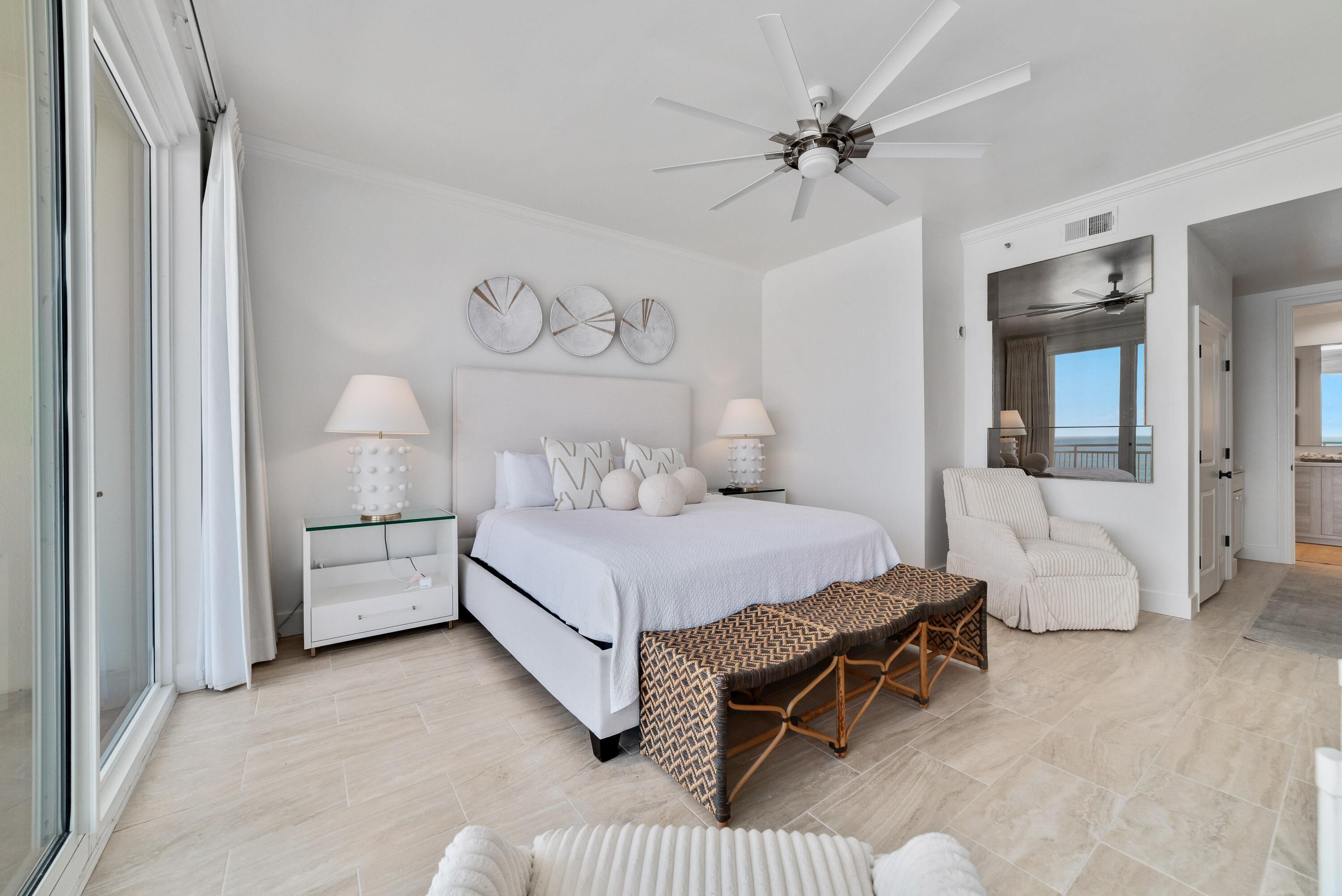 A modern bedroom with a large bed, bedside tables, a bench, and a ceiling fan.