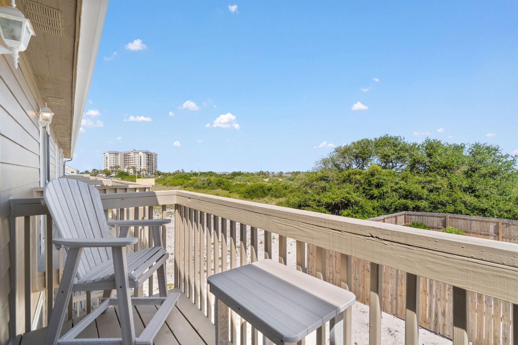 A wooden deck with a chair and a small table, overlooking a beach and a distant building.