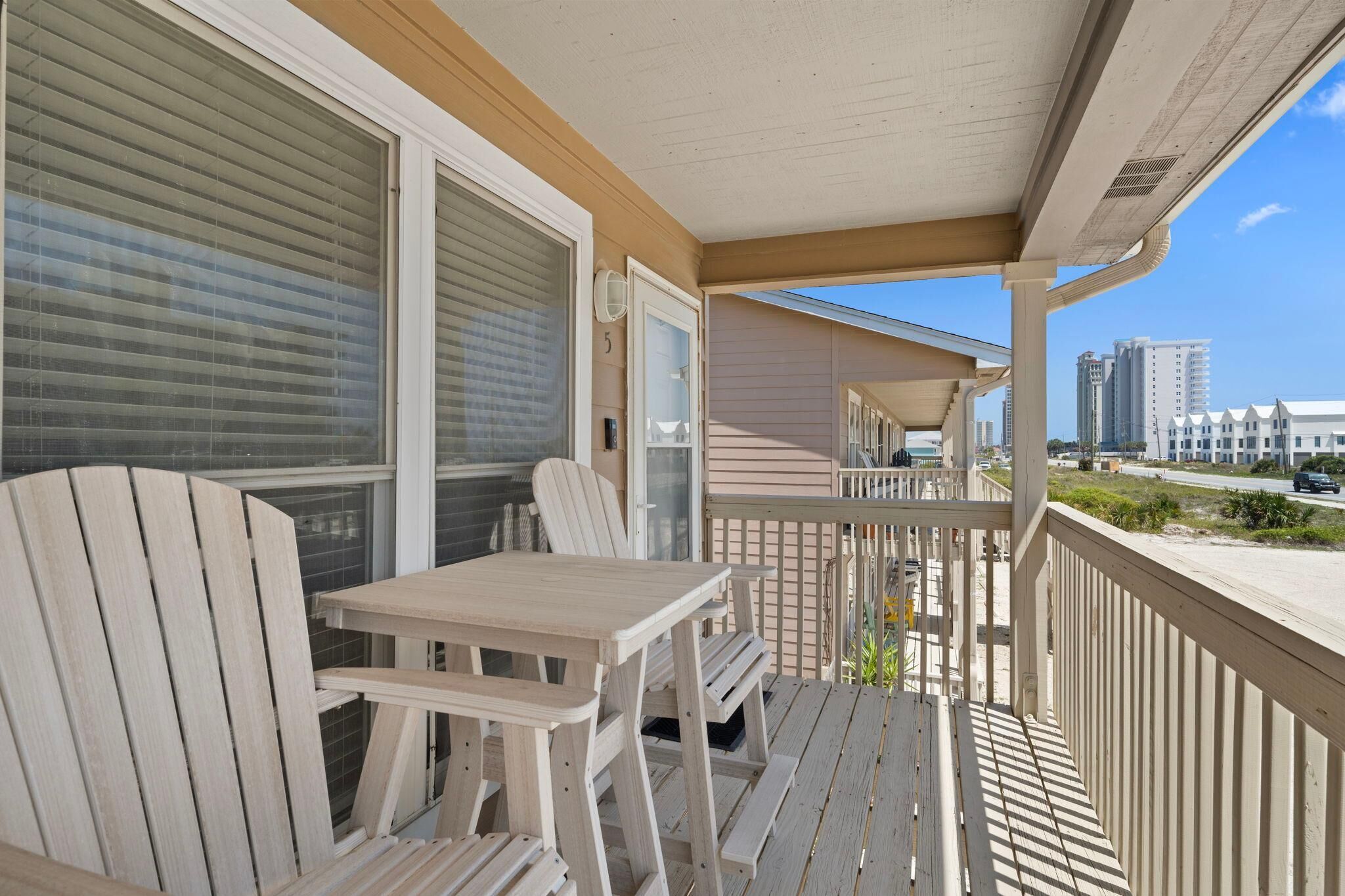 A wooden deck with a table and chairs, overlooking a beach and high-rise buildings.