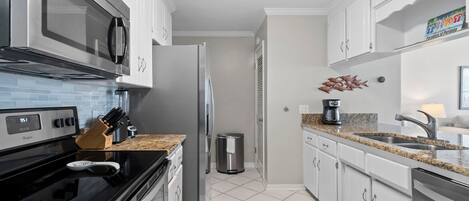 A modern kitchen with white cabinets, a stainless steel refrigerator, a microwave, and a black stove.