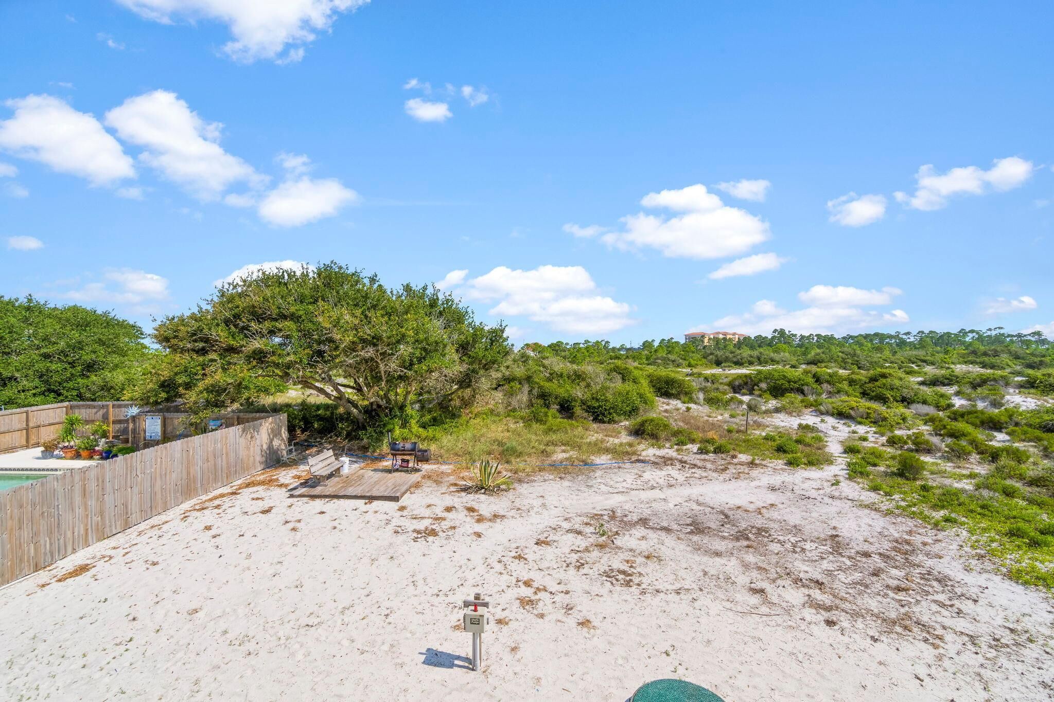 A sandy beach with a wooden deck and a tree.