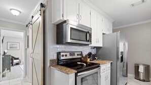 A modern kitchen with white cabinets, a stainless steel refrigerator, a microwave, and a stove. - Shore Break (Pensacola)