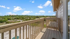 A wooden deck with a view of a beach and distant buildings. - Shore Break (Pensacola)