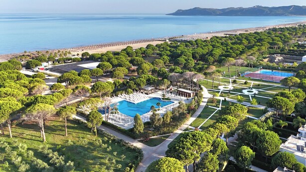 An aerial view of a resort with a large swimming pool, lush greenery, and a beach. - Perla Penthouse (Ishëm)