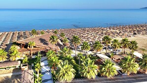 A beach resort with rows of sun loungers and thatched umbrellas, palm trees, and a view of the sea. - Perla Penthouse (Ishëm)