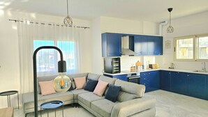 A modern kitchen with blue cabinets, a grey sofa with cushions, and a pendant light. - Perla Penthouse (Ishëm)