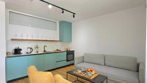 A modern kitchen with teal cabinets, a gray sofa, and a coffee table with a tray of pastries. - Aqua Bliss Apartment 296 (Ishëm)