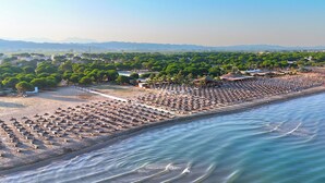 An aerial view of a beach with rows of umbrellas and beach chairs, a clear sky, and distant mountains. - Aqua Bliss Apartment 296 (Ishëm)
