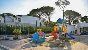 A playground with a slide and climbing structures, surrounded by a paved area and a small blue house-like structure. - Aqua Bliss Apartment 296 (Ishëm)