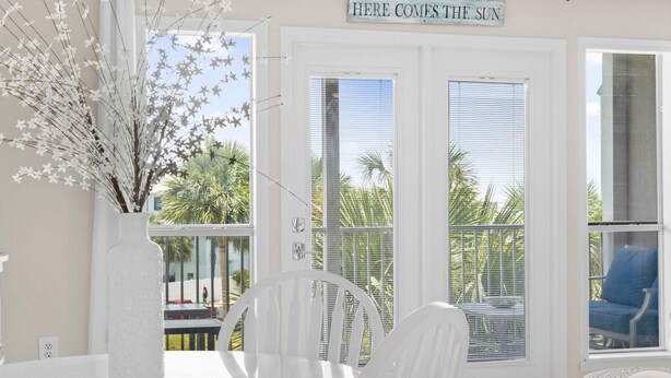 Une pièce lumineuse avec une porte blanche, une chaise blanche et un vase blanc posé sur une table.