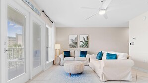 Un salon avec un canapé blanc, un pouf rond et deux lampes fixées au mur.