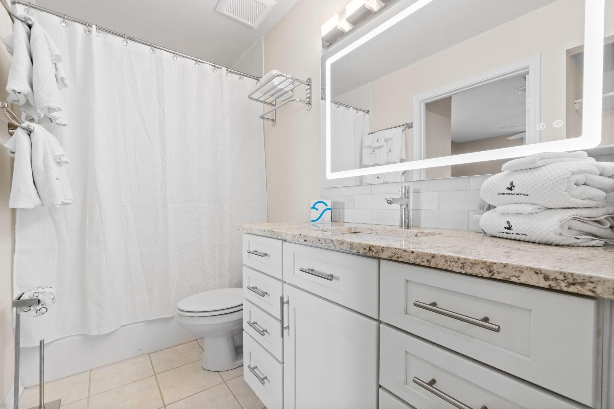 A modern bathroom with a shower curtain, a toilet, a sink with a mirror, and a towel rack with folded towels.