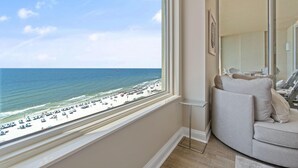 Una habitación con un amplio ventanal con vistas a la playa, un sofá gris curvo y una mesita auxiliar.