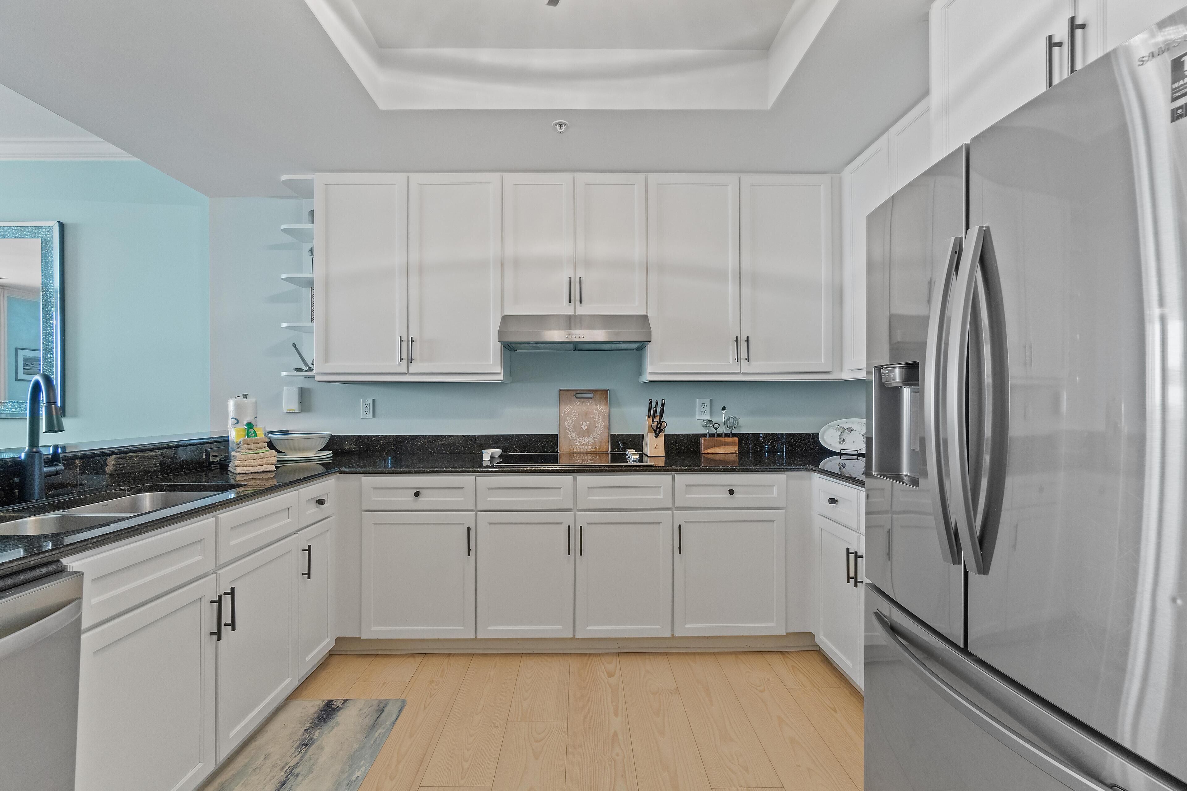 A modern kitchen with white cabinets, a stainless steel refrigerator, and a black countertop.