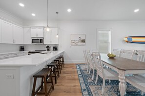 Een moderne keuken met witte kasten, een centraal eiland met barstoelen en een eethoek met een houten tafel en stoelen.