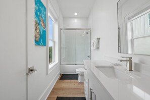 Een moderne badkamer met een douchecabine van glas, een wit toilet en een grote spiegel boven de wastafel.