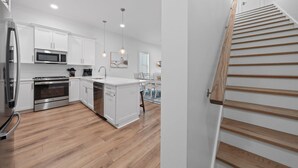A modern kitchen with white cabinets, stainless steel appliances, and wooden flooring. - Totally Beachin' at Pelican Place (Gulf Shores)