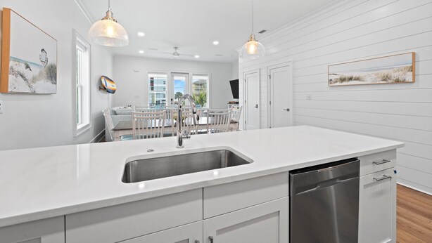 A modern kitchen with white cabinetry, a large island with a sink, pendant lighting, and artwork on the walls. - Totally Beachin' at Pelican Place (Gulf Shores)