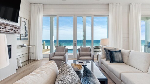 Ein modernes Wohnzimmer mit großem Fenster zum Meer, einem flachbildfernseher an der Wand und einer gemütlichen Sitzecke mit Sofa und Sesseln.