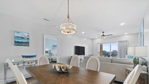 A modern living room with a wooden dining table, white chairs, a sofa, and a ceiling fan. - Riviera Dunes 302 (Pensacola)