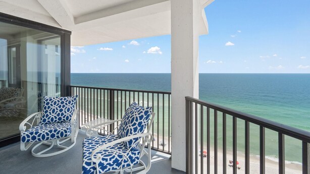 A balcony with two rocking chairs and a glass door leading to a beach view. - Broadmoor 1105 (Orange Beach)