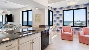 A modern kitchen with a large island, built-in dishwasher, and a dining area with pink chairs. - Broadmoor 1105 (Orange Beach)