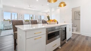 A modern kitchen with white cabinetry, stainless steel appliances, and a central island with fruit. - The Bluffs #6 - Coastal Bliss (Orange Beach)