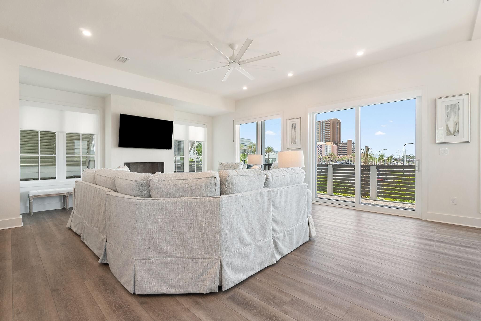 A spacious living room with a sectional sofa, a flat-screen TV, and large windows offering a view of buildings and greenery.