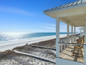 A beach view from a covered area with a wooden deck and chairs. - Shipfaced Beach House (Gulf Shores)