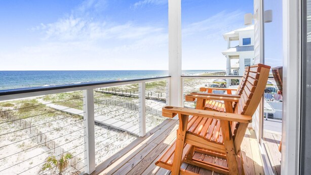 Ein Balkon mit Holzstühlen, Blick auf den Strand und ein Gebäude im Hintergrund.