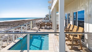 Ein Poolbereich mit Blick auf den Strand, mit Holzterrasse und Liegestühlen.