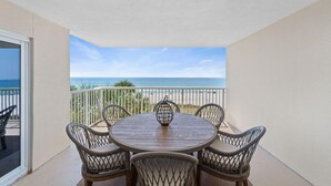 Une table ronde en bois, entourée de quatre chaises en osier, sur un balcon offrant une vue sur l’océan.