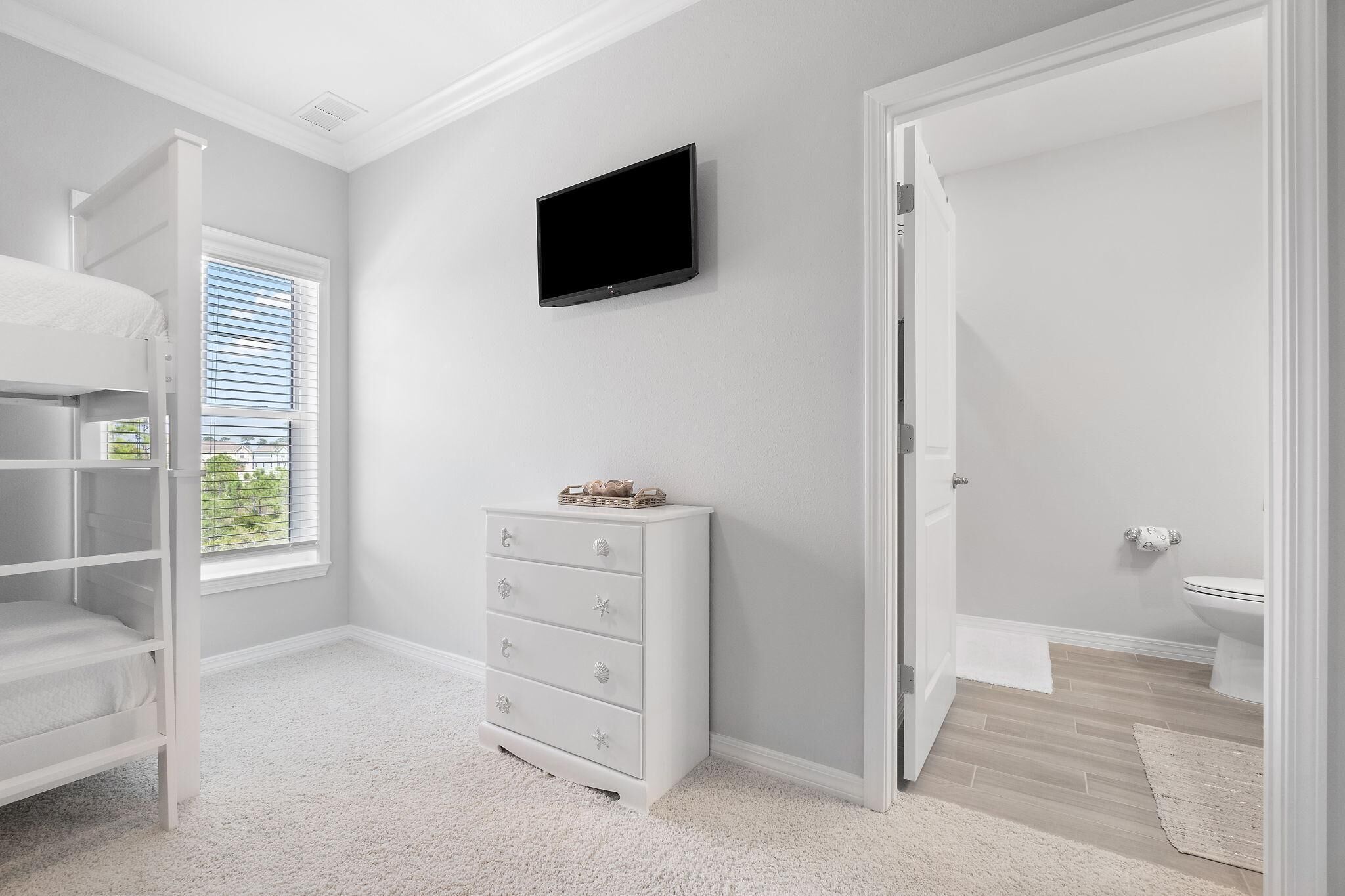 Een kamer met een stapelbed, een witte ladekast, een televisie en een deur naar een badkamer.