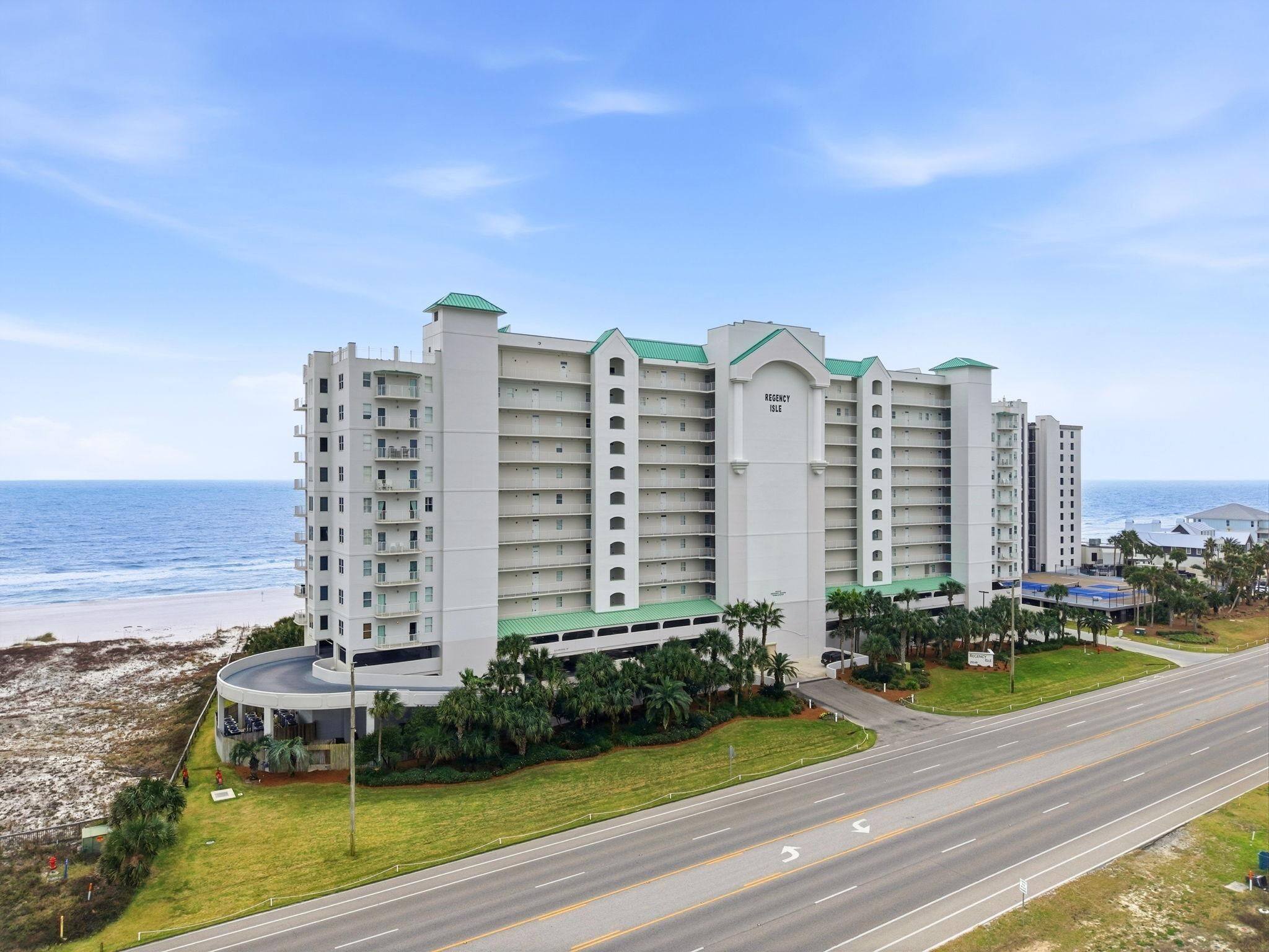 A multi-story hotel with a central courtyard, located near a beach and a road.