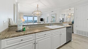 A modern kitchen with granite countertops, white cabinetry, a double sink, and a dishwasher.