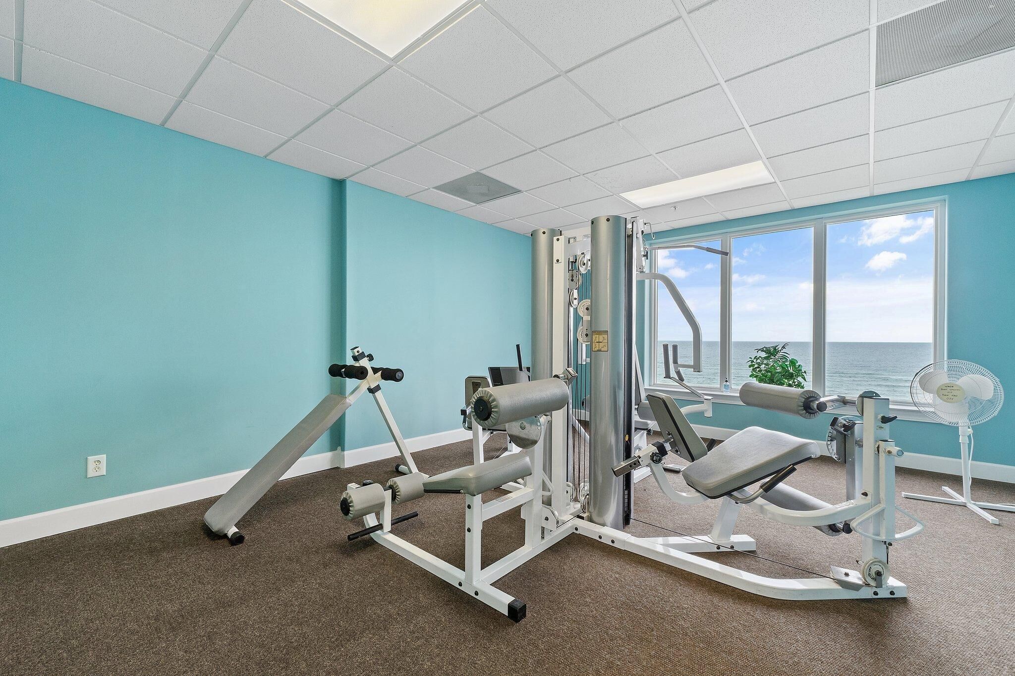 A gym with exercise equipment, a large window, and a view of the ocean.