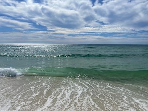 A beach with clear water and waves, under a partly cloudy sky.
