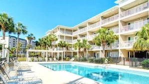 A hotel with a swimming pool, multiple balconies, and palm trees.