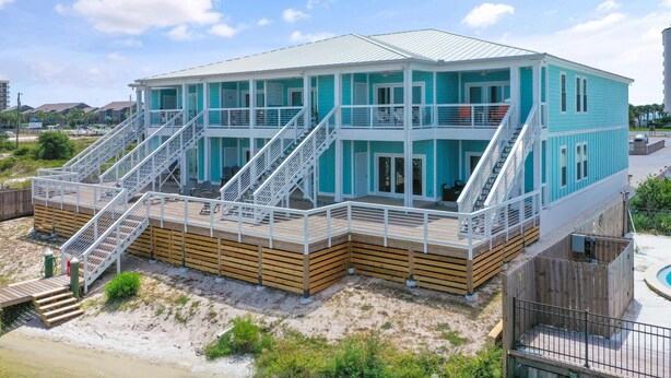 Casa frente al mar de dos pisos con un porche de madera y una escalera que lleva al nivel superior.