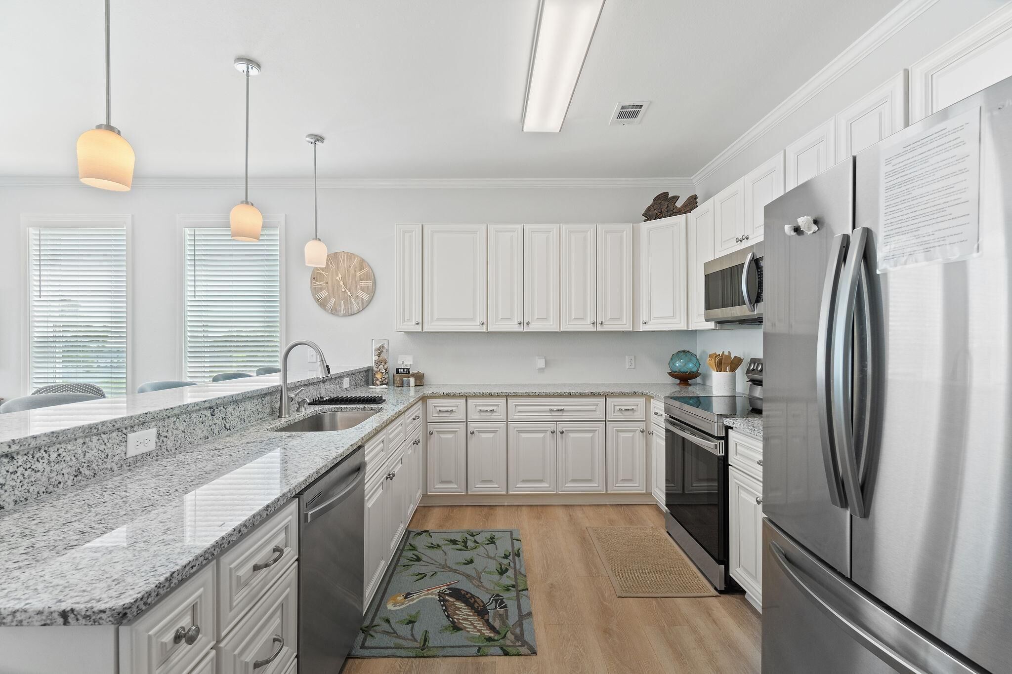 A modern kitchen with white cabinets, a stainless steel refrigerator, granite countertops, and pendant lighting.