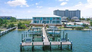 Un hotel frente al agua con un muelle que se adentra en el agua, un edificio grande con varios balcones y un área de piscina.