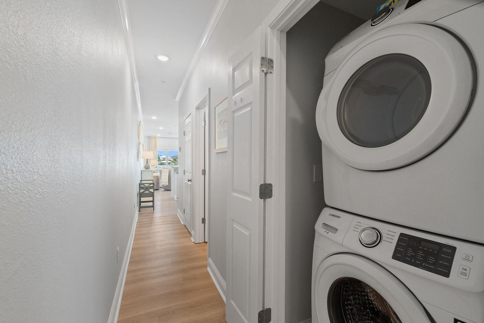 Une buanderie avec des machines à laver et des sèche-linge superposés, un plancher en bois et des murs blancs.