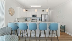 Una cocina moderna con armarios blancos, un refrigerador de acero inoxidable, un microondas y una isla grande con taburetes de bar.