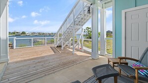 Una terraza cubierta con vista a un cuerpo de agua, barandas blancas y mobiliario exterior.