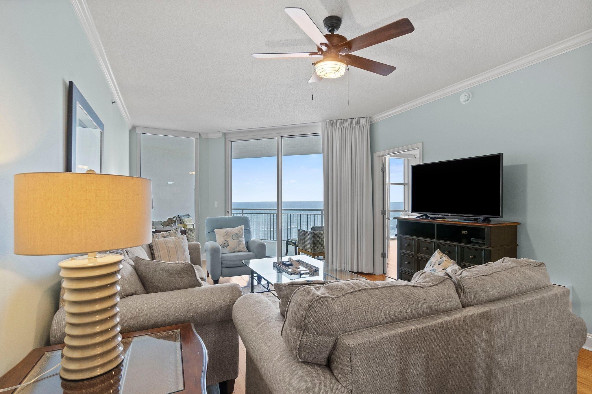 Una sala de estar con ventilador de techo, televisor y vista al mar.