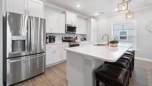 A modern kitchen with white cabinetry, stainless steel appliances, a central island with bar stools, and pendant lighting. - Slow M'ocean at Lost Key Villas (Pensacola)