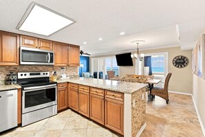 A kitchen with wooden cabinets, stainless steel appliances, and a large island. - Castaways 5D (Gulf Shores)