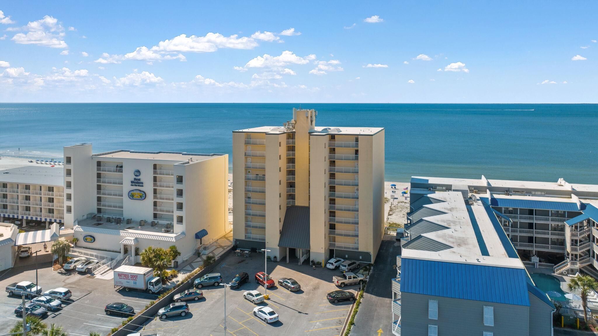 A hotel with multiple floors, a parking lot, and a view of the ocean.