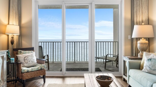 A room with a view of the sea, a wicker chair, a sofa, and a table with a bowl. - Windemere 602 (Pensacola)